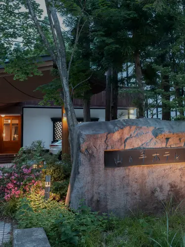 木造の重厚な建物が特徴的なホテル。雪が積もった冬の夜、暖色の照明が灯り、温かみのある雰囲気を醸し出している。