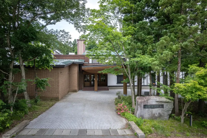 冬の情景に佇む木造の旅館。石に刻まれた館名の看板がライトアップされ、落ち着いた雰囲気を醸し出している。