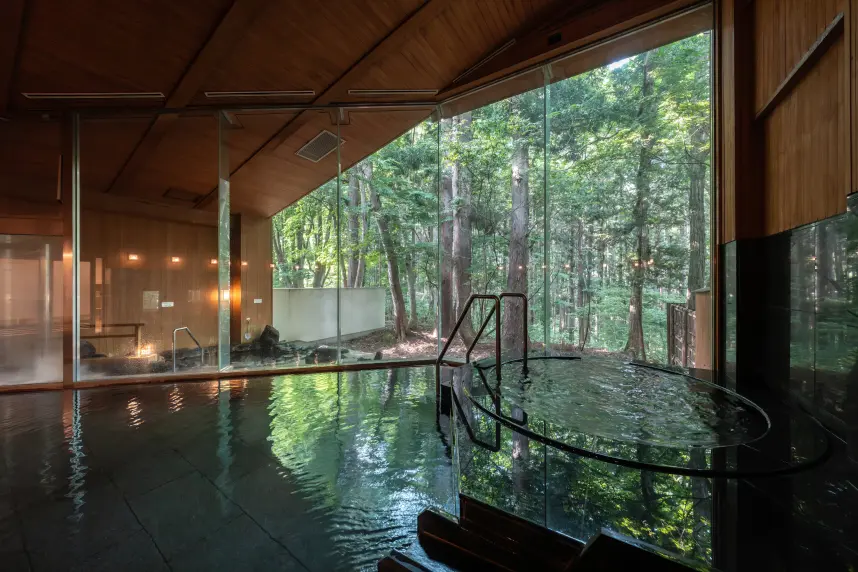 大きな窓から自然の景色を眺められる温泉の内風呂。木の温もりを感じる天井と黒い湯船が落ち着いた雰囲気を演出している。